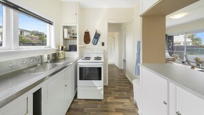 A modern kitchen with white cabinets, a stainless steel countertop, and a wood floor. - The Green Trout - Paraparaumu Beach Holiday Home (Paraparaumu Beach)