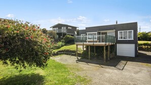 A modern two-story house with a balcony, a garage, and a well-maintained garden with red flowers. - The Green Trout - Paraparaumu Beach Holiday Home (Paraparaumu Beach)