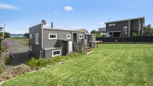 A modern two-story house with a well-maintained lawn and a satellite dish. - The Green Trout - Paraparaumu Beach Holiday Home (Paraparaumu Beach)