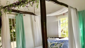 A four-poster bed with white bedding, a ceiling fan, and a window with curtains.