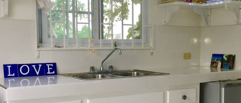 Una cocina con armarios blancos, un lavamanos de acero inoxidable y una ventana con cortinas.