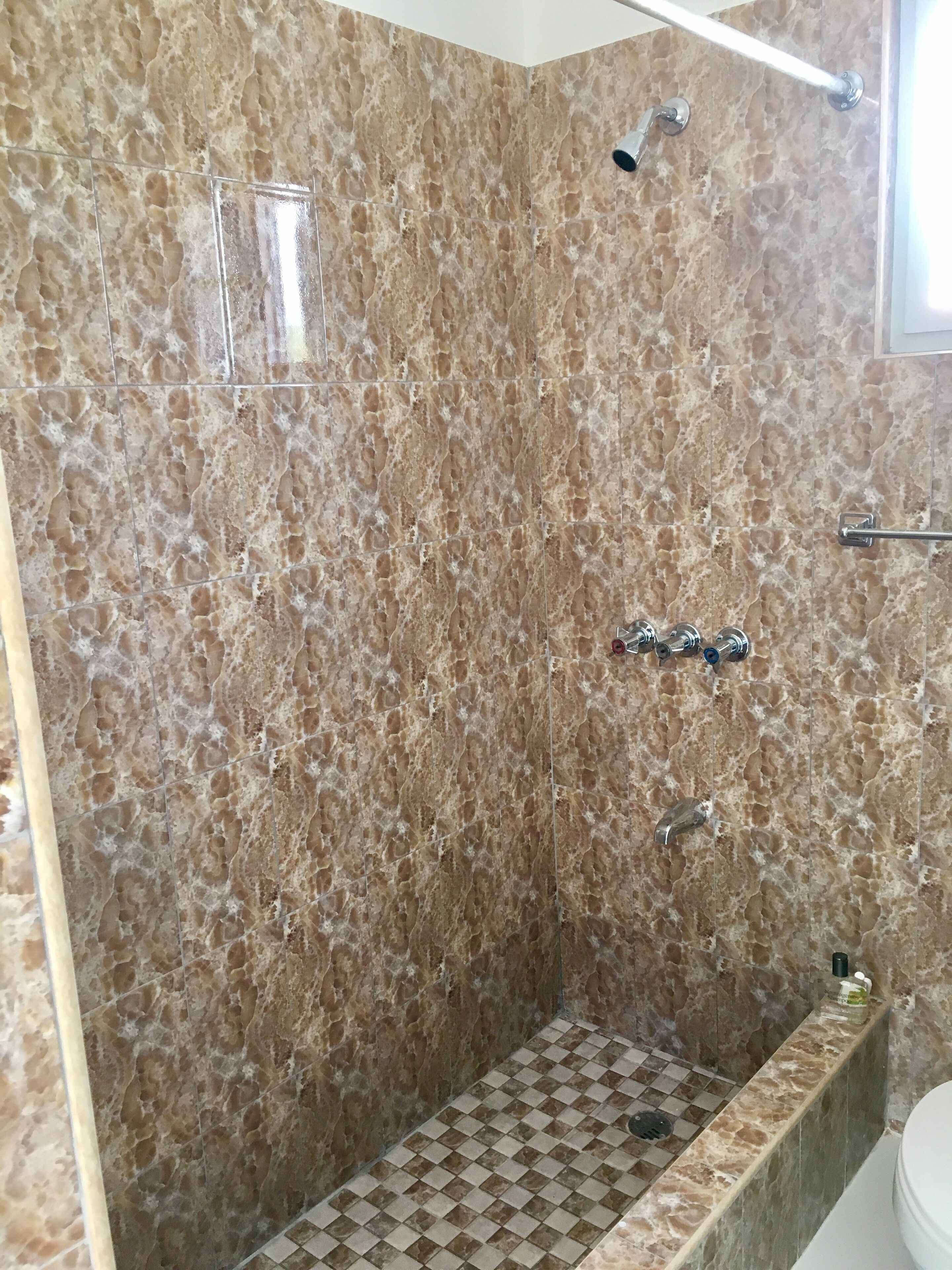 A bathroom with a shower area featuring a checkered floor and a marble wall.