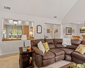 A spacious living room with a brown leather sectional sofa, a small wooden side table, and a mirror on the wall.