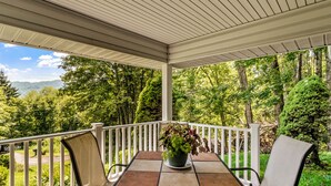 A covered outdoor seating area with a table and chairs, surrounded by a white railing, overlooking a forested landscape. - Walk to Ski Lodge..Mountain Views..Includes Ski Lodge Locker (Sugar Mountain)