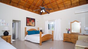 Een slaapkamer met een houten bed, een plafondventilator, een raam met gordijnen, een dressoir en een spiegel.