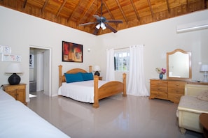 Una camera da letto con un letto in legno, una ventola a soffitto, una finestra con tende, un comò e uno specchio.