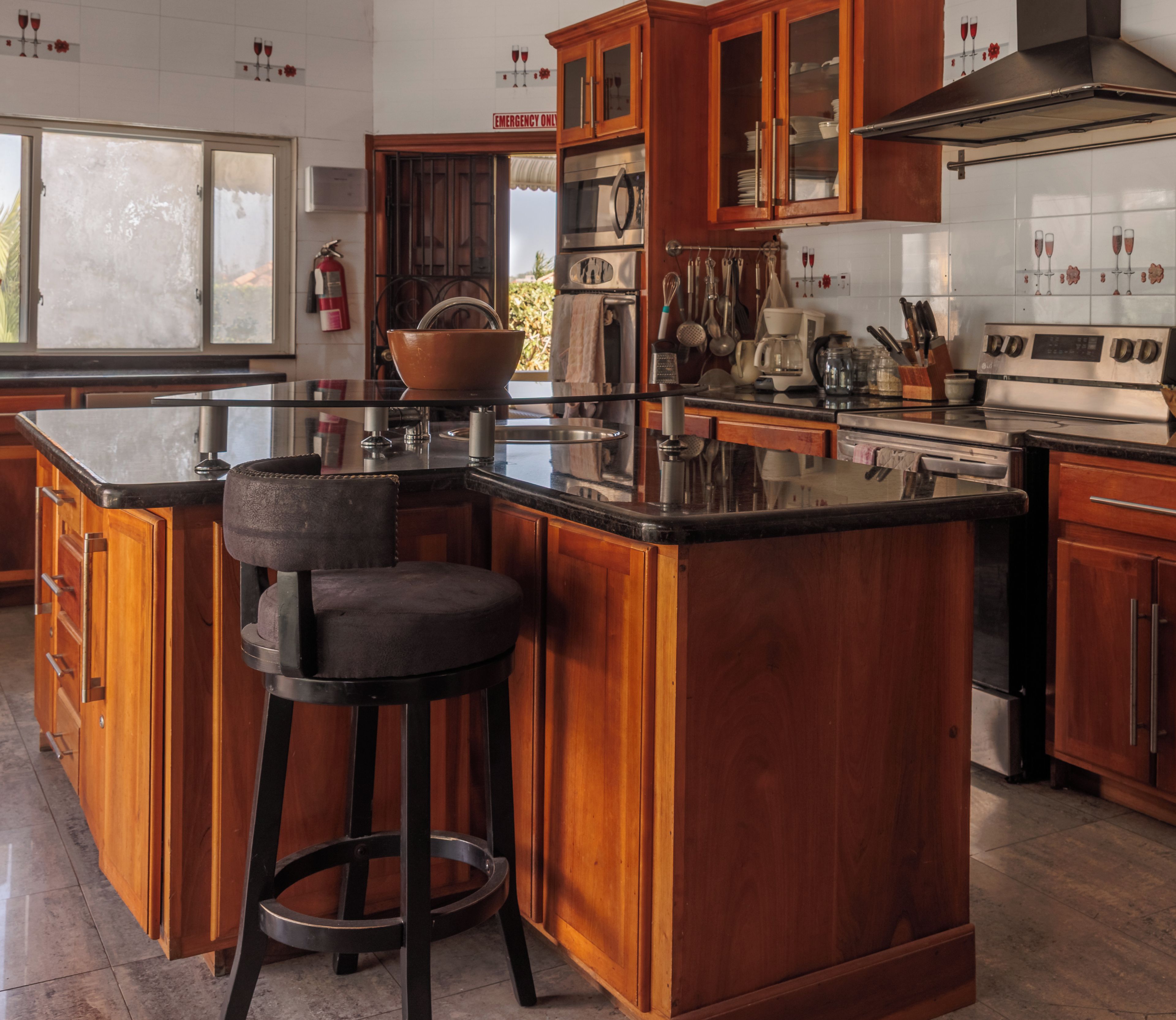 A kitchen with wooden cabinets, a central island with a bar stool, stainless steel appliances, and a tiled backsplash.