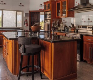 A kitchen with wooden cabinets, a central island with a bar stool, stainless steel appliances, and a tiled backsplash.