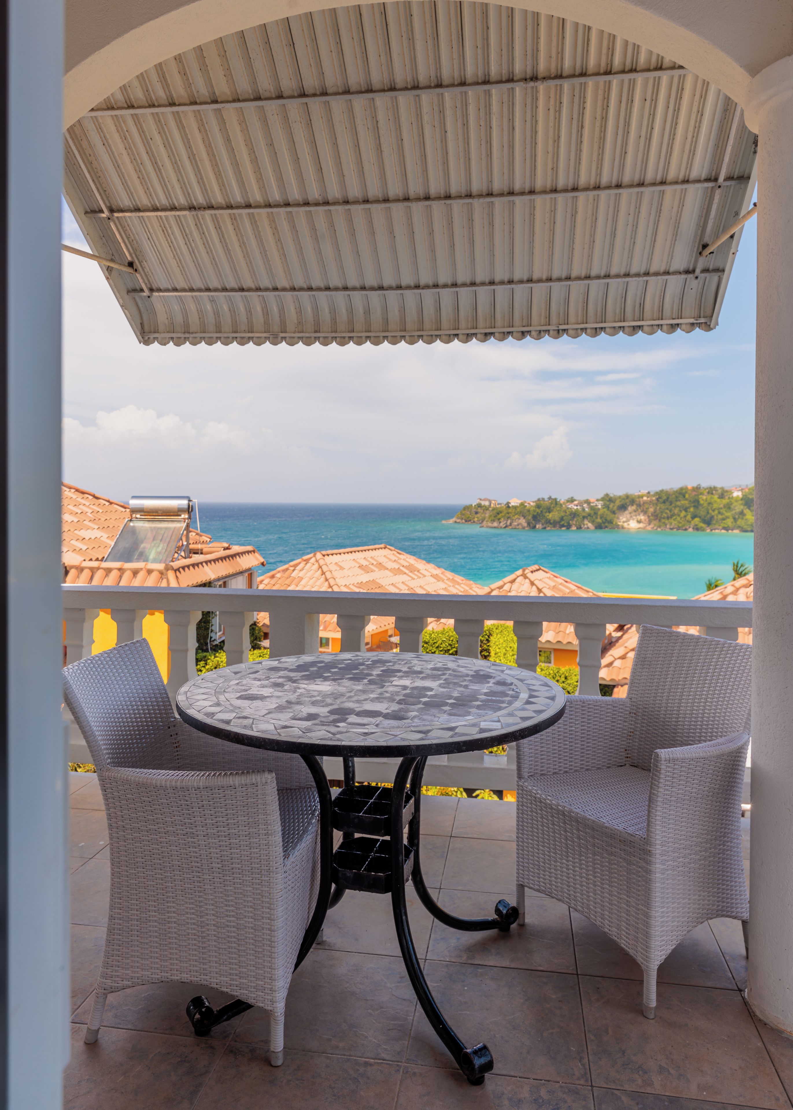 A covered outdoor seating area with a table and two chairs, overlooking a coastal view.