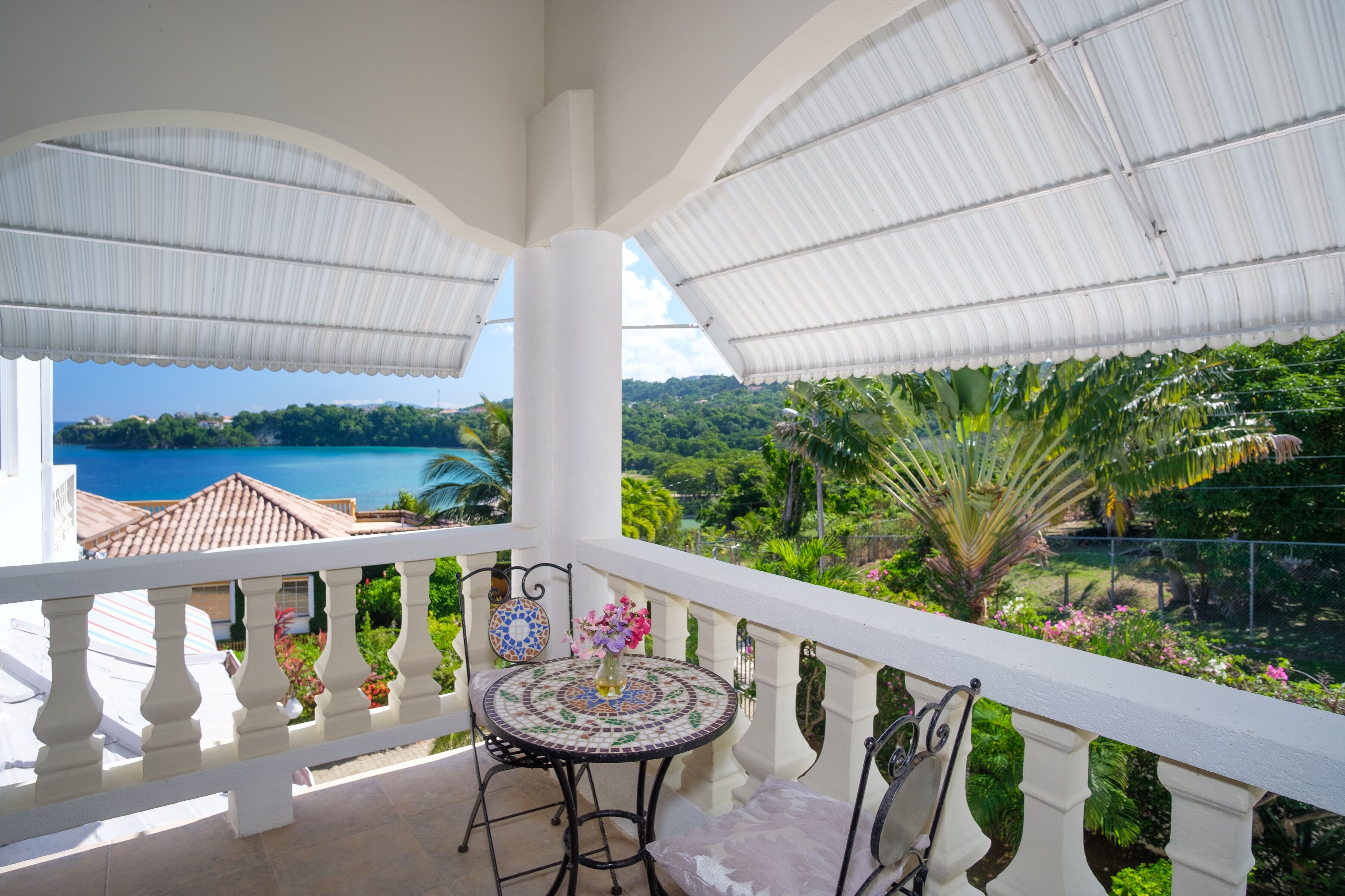 Un balcon donnant sur un jardin luxuriant et un plan d’eau.
