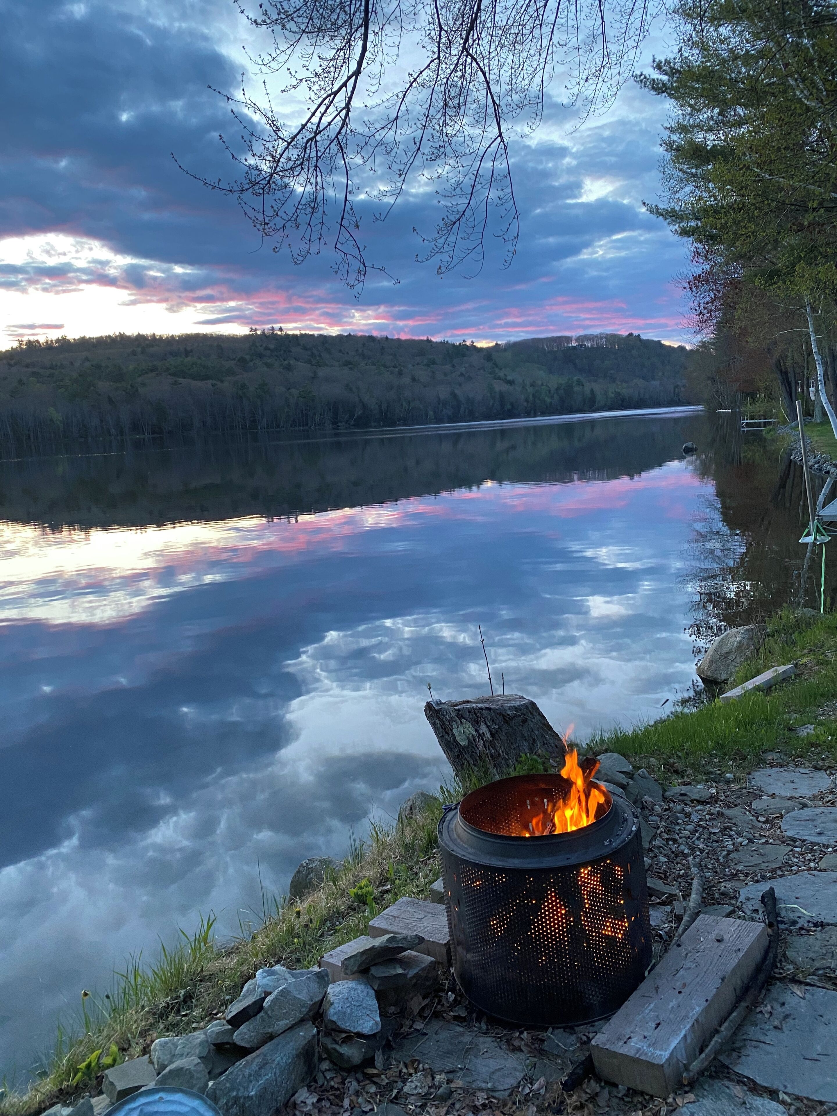 Una fogata junto a un lago tranquilo, con un bosque al fondo.