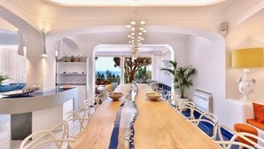 Un espace repas moderne avec une longue table en bois, des chaises blanches et une vue sur l’extérieur.