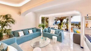 Un salon moderne avec un canapé d’angle bleu, une table basse en verre et une vue sur l’extérieur.