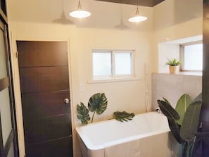 A bathroom with a bathtub, two pendant lights, a window, and a potted plant.
