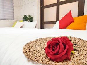 A neatly made bed with a woven placemat and a single red rose.