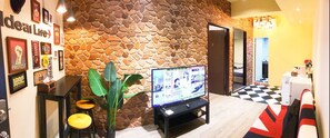 Un vestíbulo con pared de piedra, un televisor mostrando un noticiero, una planta pequeña y un piso a cuadros.