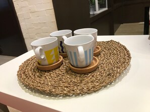 Una mesa con cuatro tazas blancas sobre posavasos, sobre un mantel tejido.