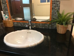 Un baño con un lavamanos blanco, un espejo y una planta en maceta.