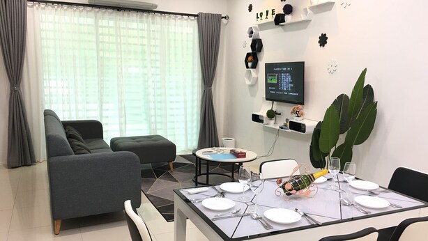 A modern living room with a grey sofa, a round dining table set for two, and a TV mounted on the wall. - Ipoh Paradise Homestay Station 18 (Ipoh)