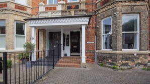A building with a brick facade, a white entrance with a porch, and a black metal fence. - Sycamore Apartments (York)