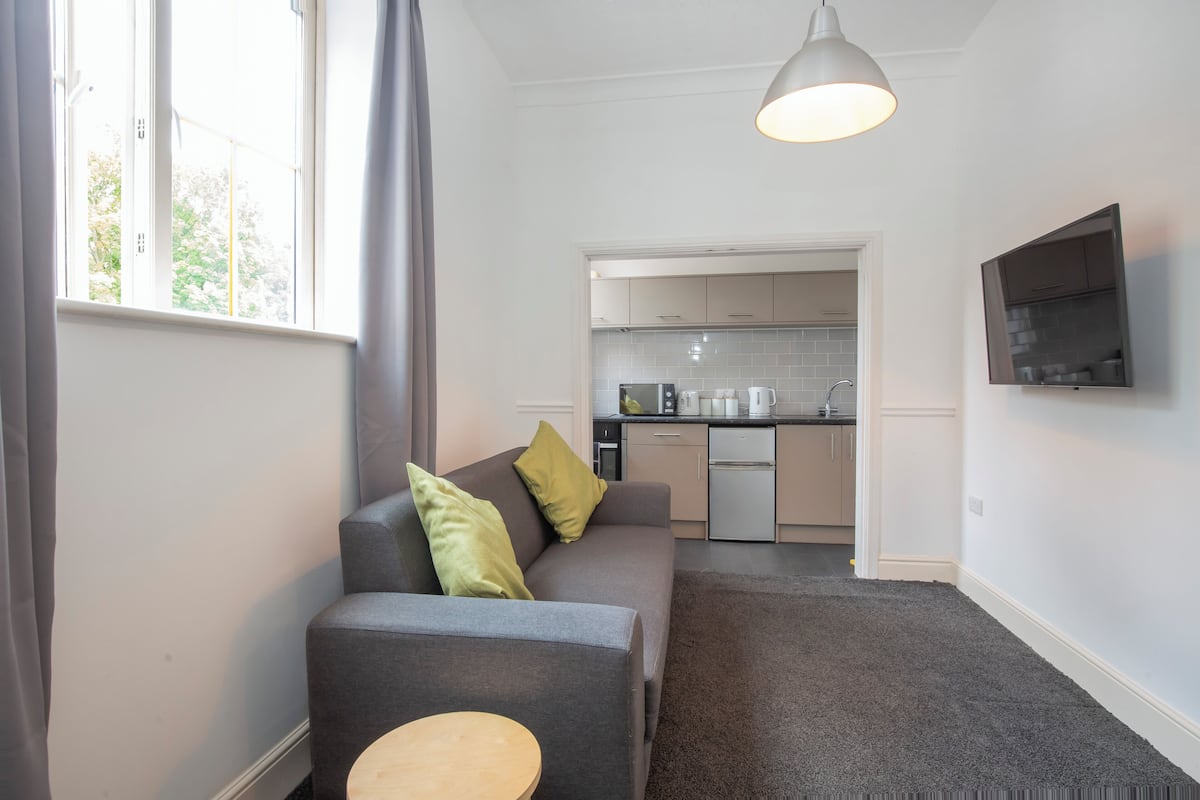 A modern living room with a grey sofa, a small round table, and a kitchen in the background.