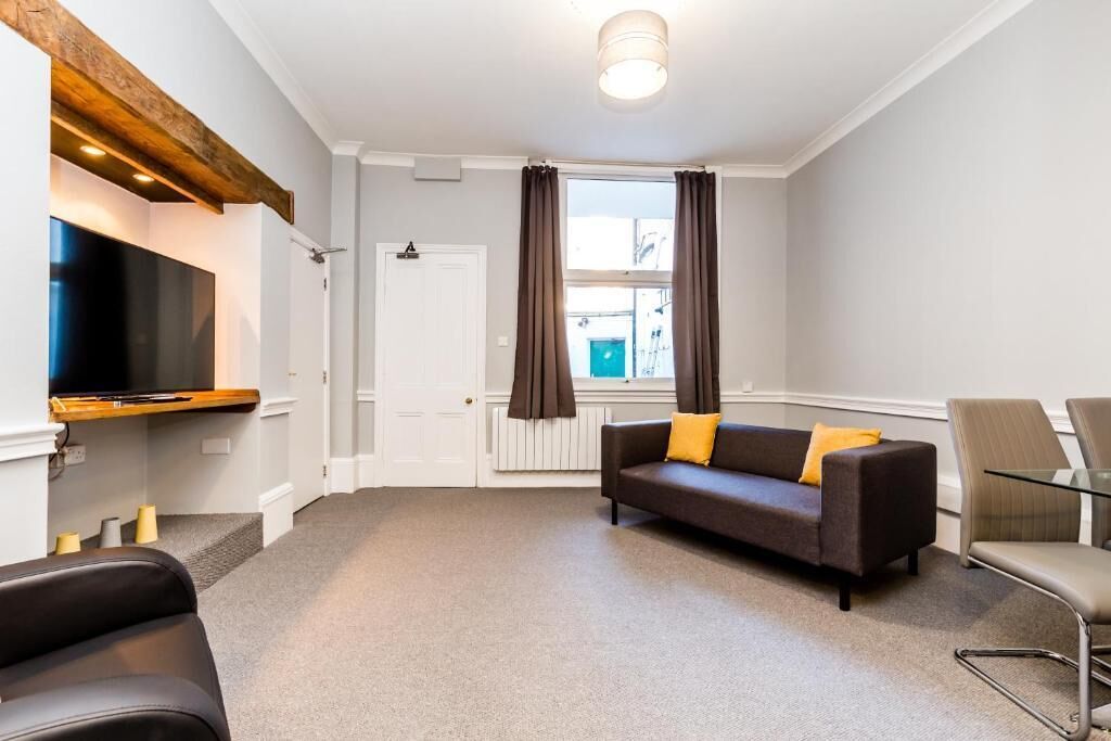 A modern living room with a flat-screen TV, a sofa with cushions, a glass coffee table, and a chair.