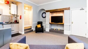 A modern living room with a grey sofa, a black armchair, and a flat-screen TV mounted on the wall. - Sycamore Apartments (York)