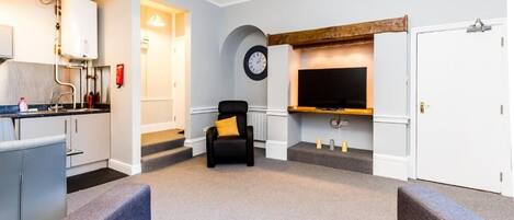 A modern living room with a grey sofa, a black armchair, and a flat-screen TV mounted on the wall.