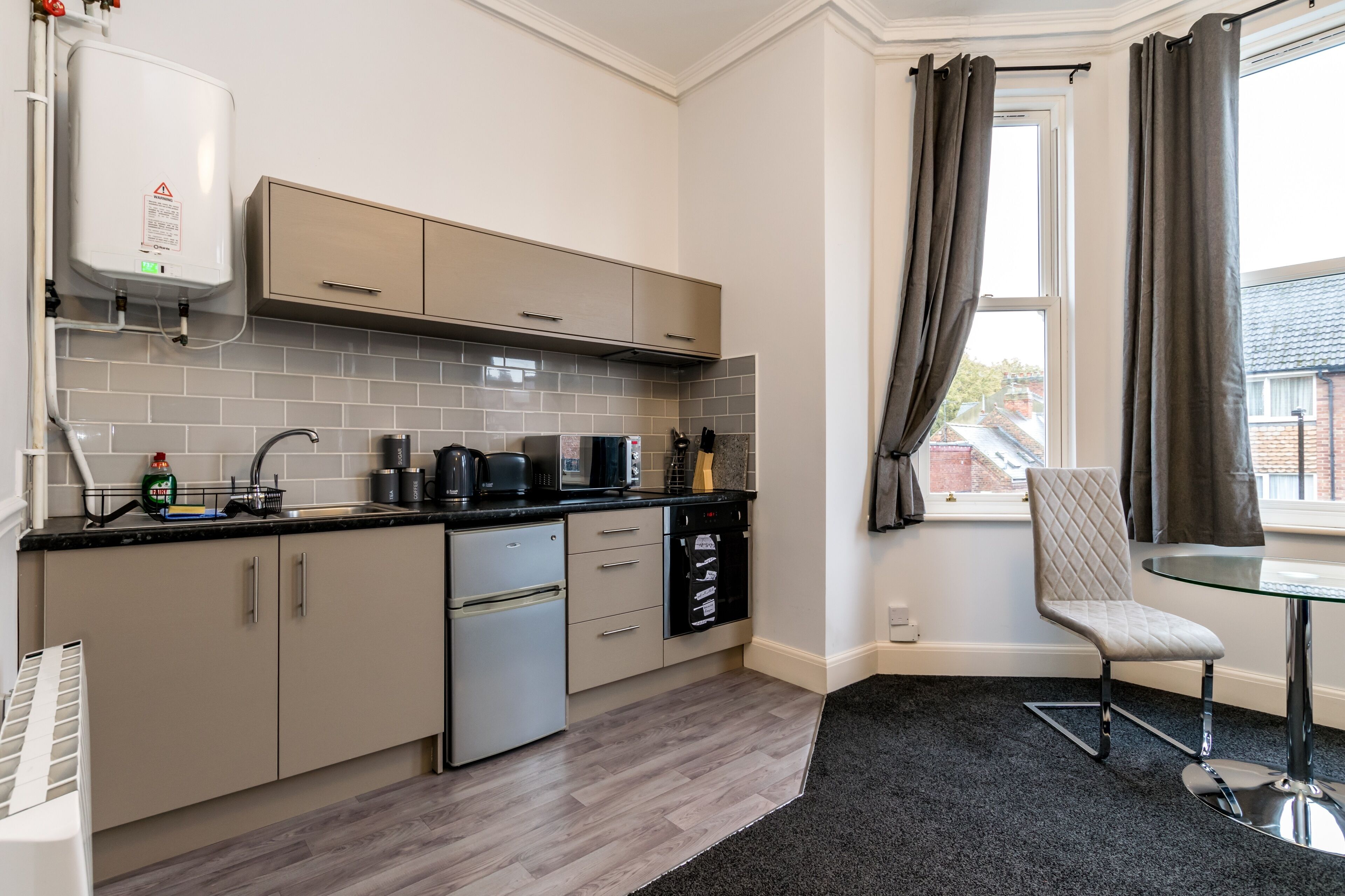 A modern kitchen with a dishwasher, stove, and microwave. There is a window with curtains and a chair near the window.