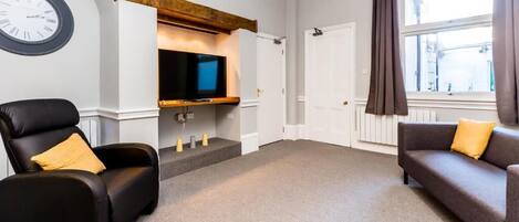 Una sala de estar moderna con un televisor de pantalla plana, una chimenea, un sillón de cuero negro, un sofá marrón y un ventanal con cortinas.