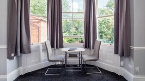 A corner room with a bay window, two chairs, a small table, and a black carpet. - Sycamore Apartments (York)