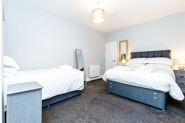 Une chambre d’hôtel avec deux lits simples, une table de chevet, une commode, un miroir et un radiateur.