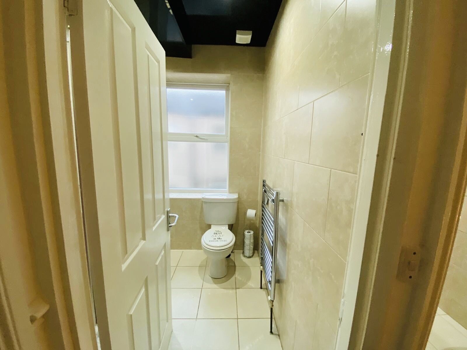 A narrow bathroom with a toilet, a window, and a towel rack.