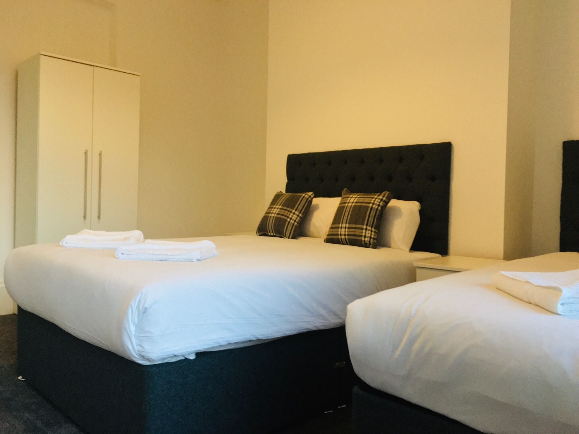 A hotel room with two beds, a wardrobe, and a headboard.