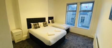 A hotel room with two beds, a small bedside table, a wardrobe, and a window with bars.