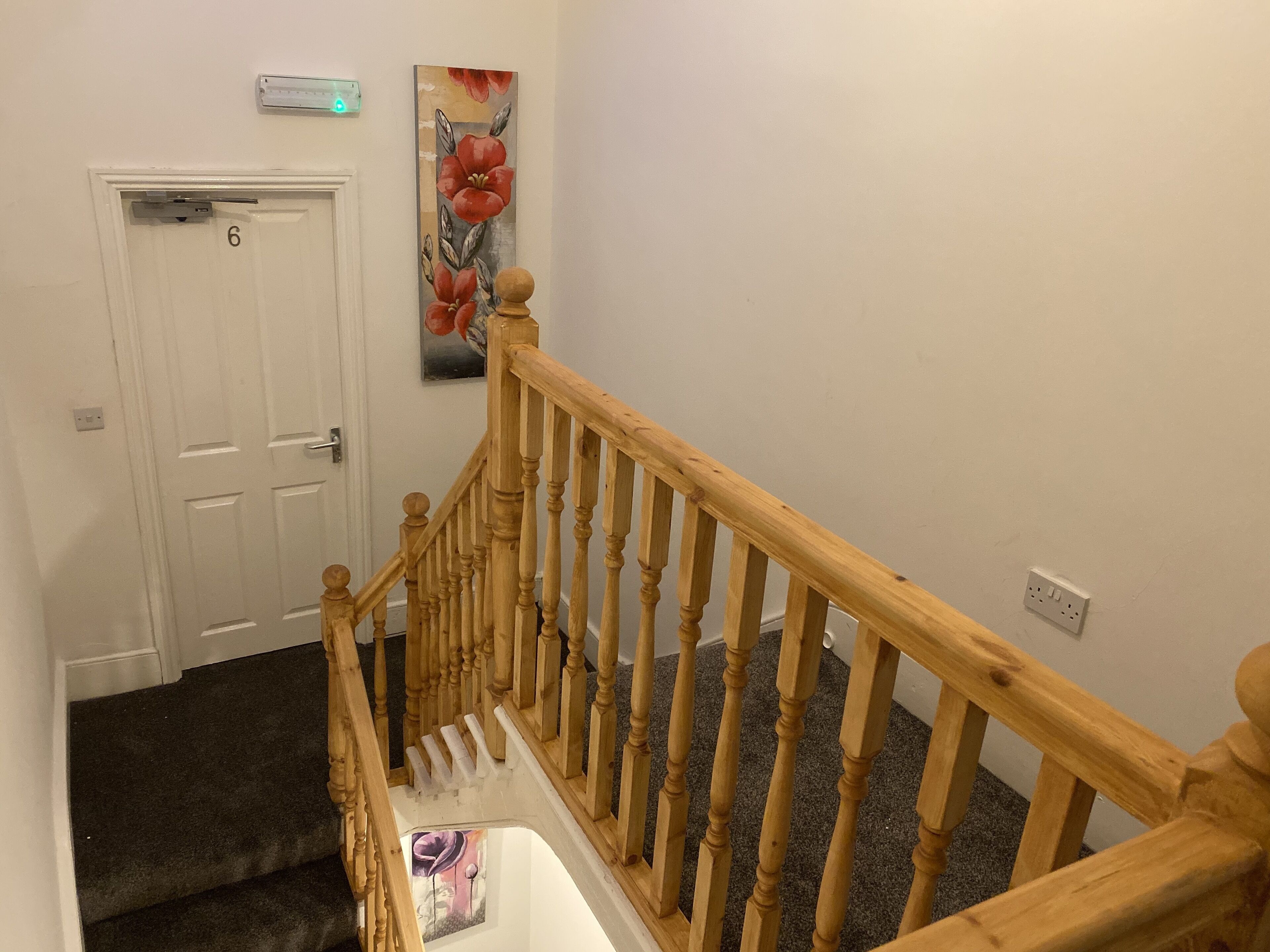 A staircase with wooden balusters and a handrail, carpeted steps, a white door with a number, and a wall-mounted light fixture.