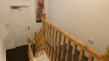 A staircase with wooden balusters and a handrail, carpeted steps, a white door with a number, and a wall-mounted light fixture.