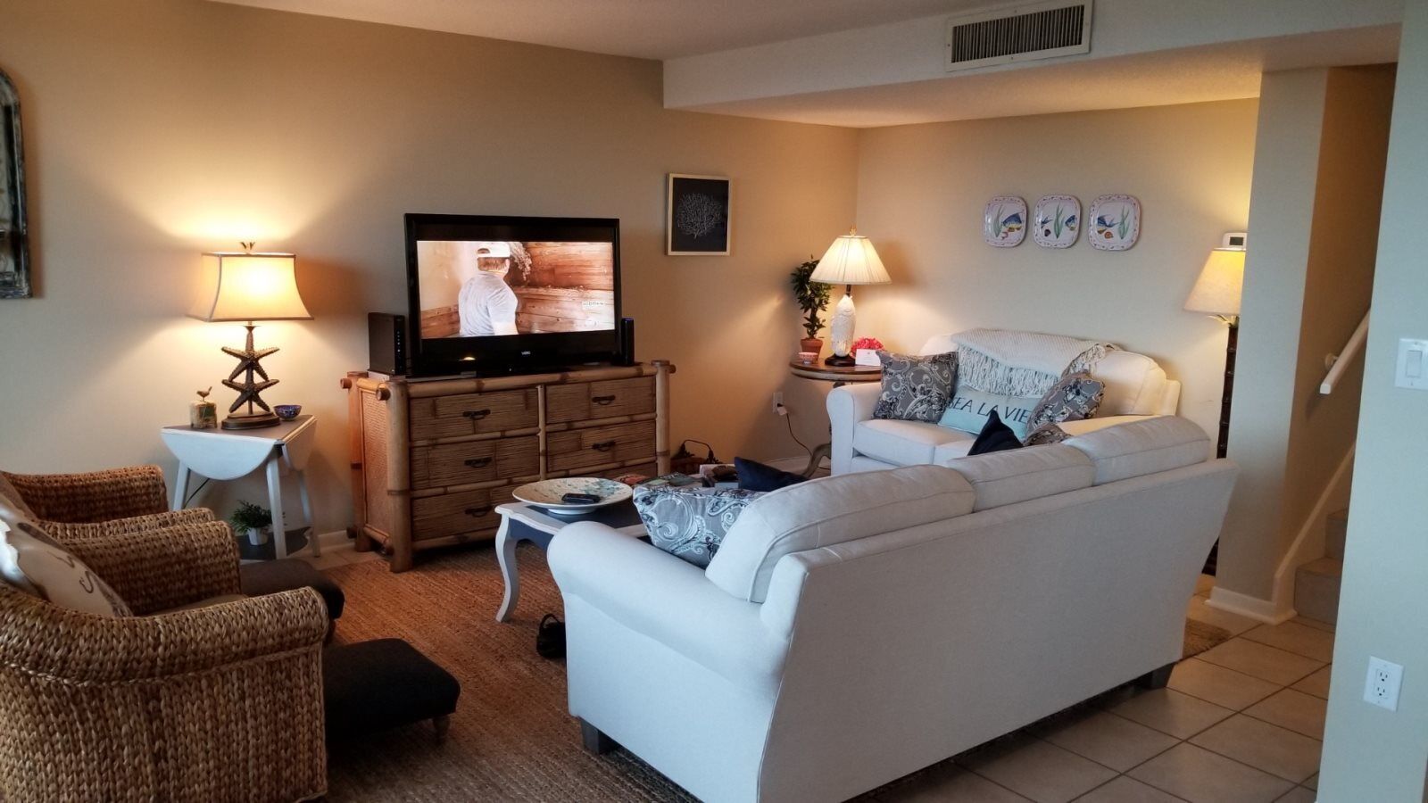 Uma sala de estar com um sofá, duas poltronas, uma televisão, uma mesa de centro e um abajur.