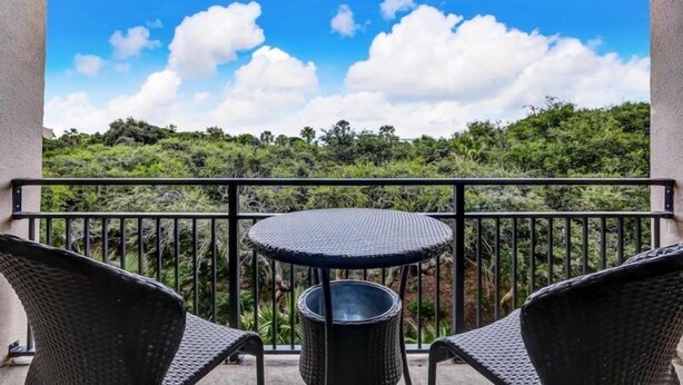 A balcony with a round table and two chairs, overlooking a lush green landscape under a clear blue sky. - 1149 Beachwalker (Fernandina Beach)