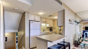 A compact kitchen with a central island, white cabinets, and a small seating area with stools. - 1149 Beachwalker (Fernandina Beach)