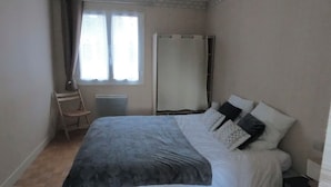 Un dormitorio con cama, una silla, un ventanal con cortinas y un armario.