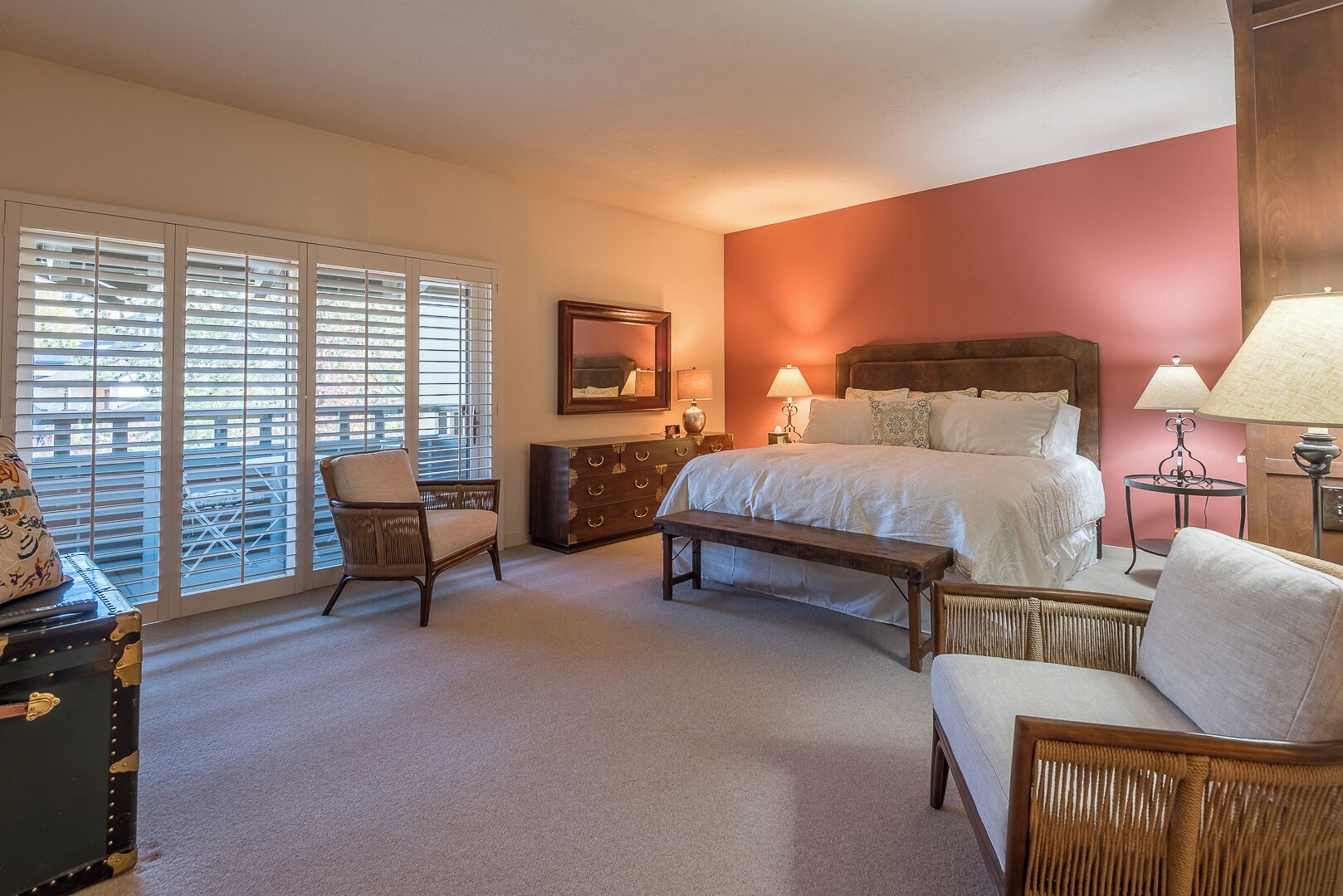 A bedroom with a large bed, two bedside tables with lamps, a chair, a bench, and a dresser.