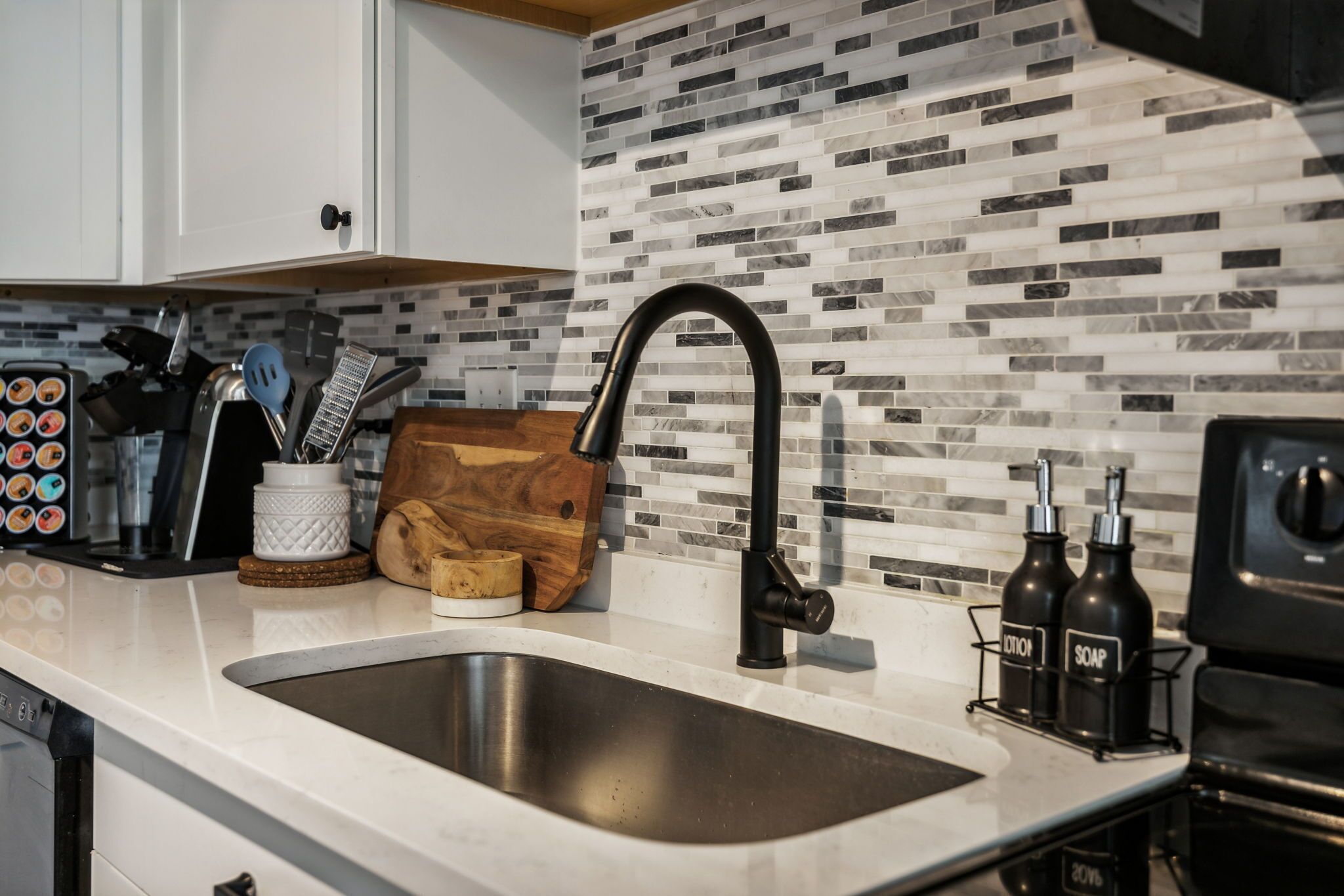Una cocina con diseño moderno, que incluye un lavamanos de acero inoxidable, un grifo negro y un salpicadero de azulejos.