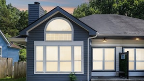 A single-story house with a dark blue exterior, a large arched window, and a garage with a light fixture.