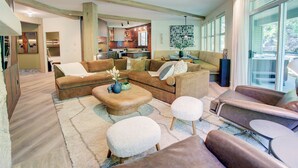 A spacious living room with a brown sofa set, a coffee table, and a dining area with a glass top table. - Designer 4BR, 3 Bath Townhouse w Mtn Views, Hot Tub, Parking for 2 vehicles (Whistler)