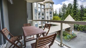 Varanda com mesa e cadeiras, vista para um edifício e uma área arborizada.