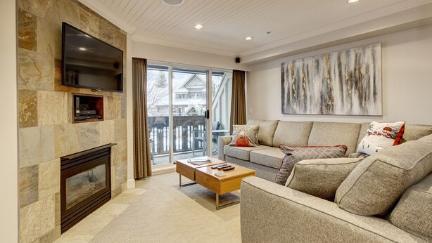 A living room with a stone fireplace, a flat-screen TV, a sofa, and a coffee table. - Heavenly 2BR/2BA. Private Hot-tub & Mountain View’s (Whistler)