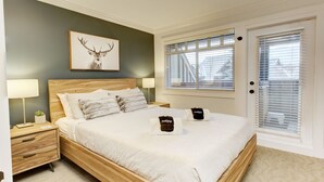 A bedroom with a wooden bed, two bedside tables, a nightstand, a wall-mounted deer artwork, and a window with blinds. - Heavenly 2BR/2BA. Private Hot-tub & Mountain View’s (Whistler)