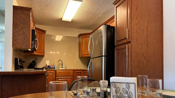 Una cocina con armarios de madera, un refrigerador de acero inoxidable y una mesa de comedor dispuesta con platos, vasos y cubiertos.