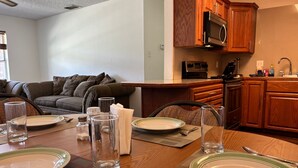 Comedor con mesa de madera dispuesta para cuatro personas, con platos, vasos y cubiertos.
